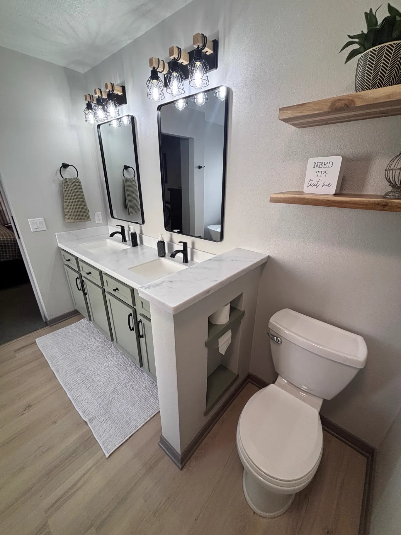 Angled view of a sage green double vanity with black cage vanity lights and floating live-edge wood shelves