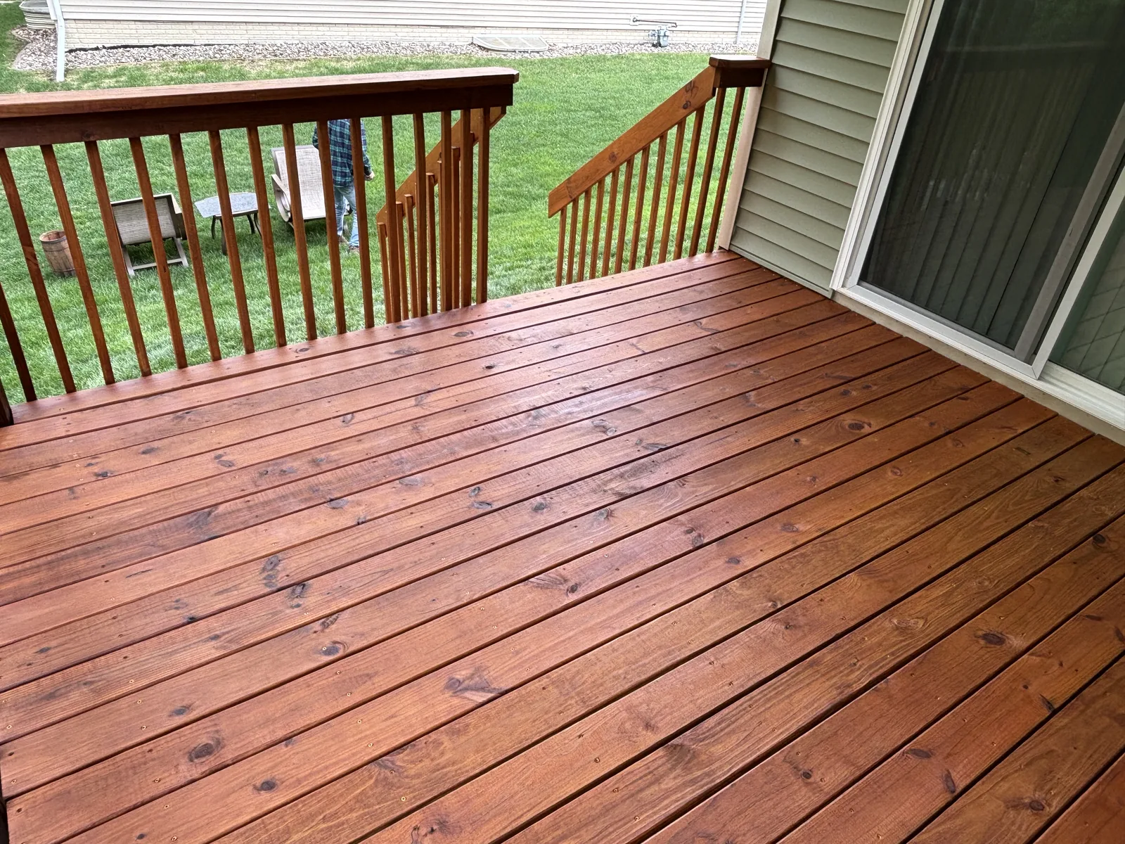Freshly stained cedar-tone deck with matching railing and sliding door access at the back of a home
