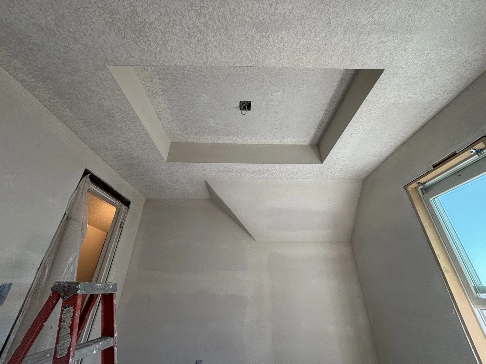 Freshly hung and textured drywall forming a stepped tray ceiling detail in a newly finished room