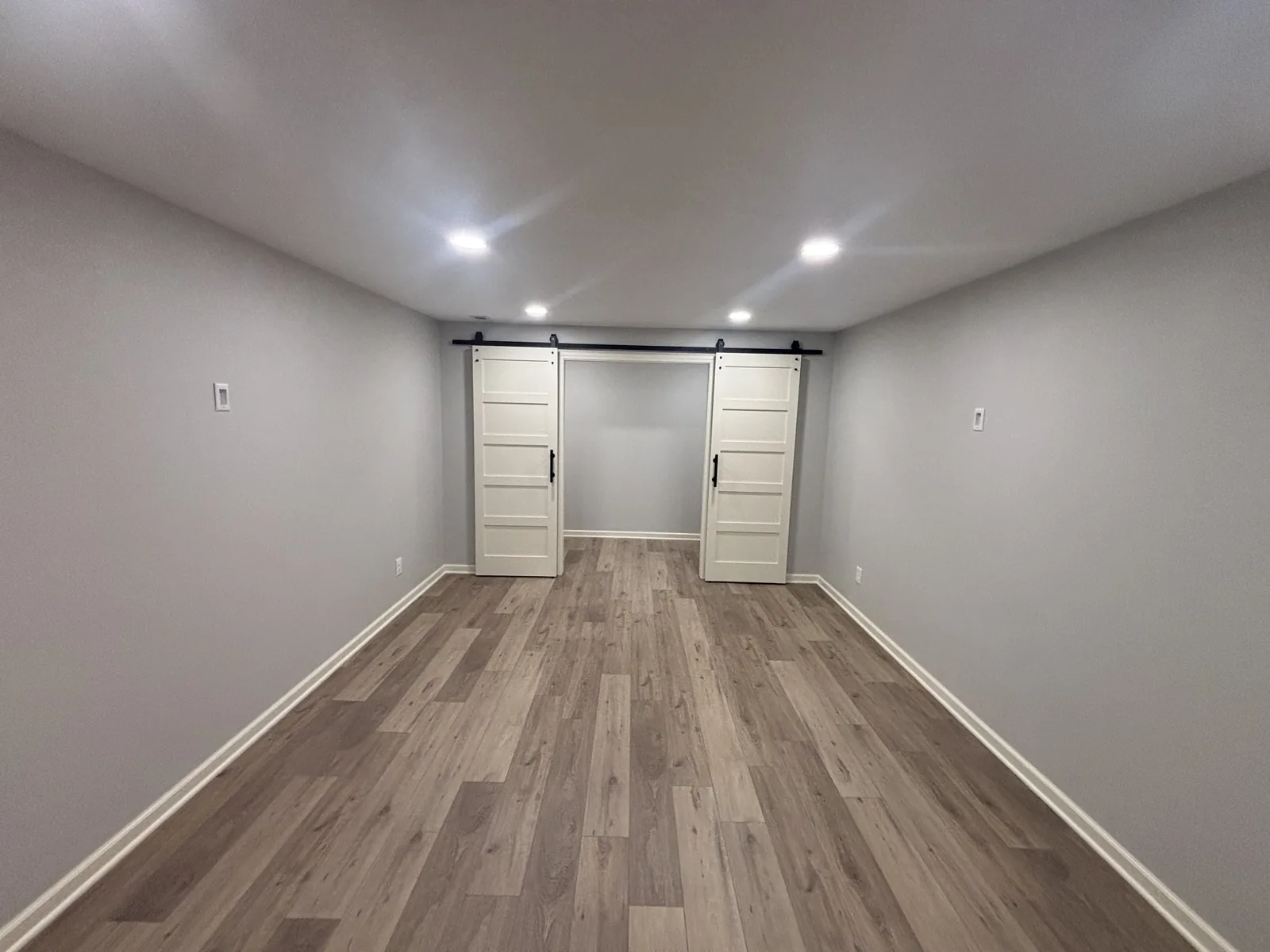 Finished basement room with painted walls, recessed lighting, wood-look plank flooring, and double white barn doors on black track