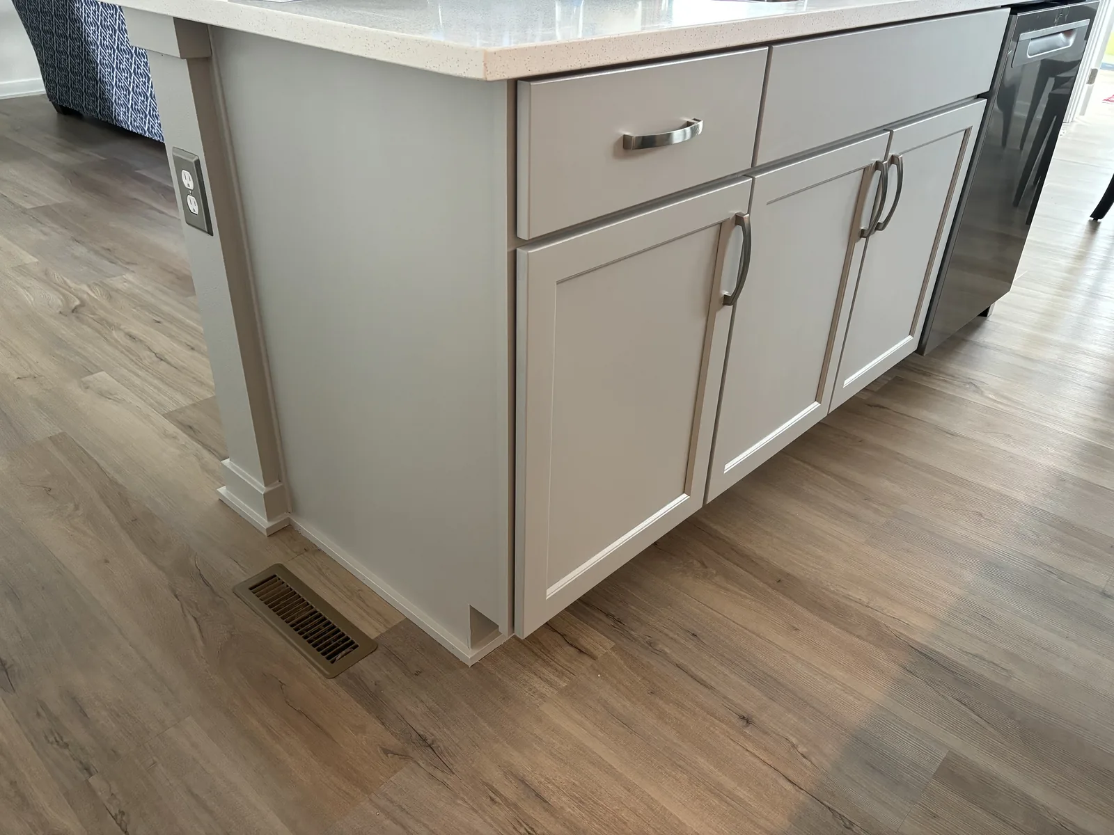 Painted kitchen island with shaker cabinet doors, quartz countertop, and decorative corner post over wood-look vinyl plank flooring