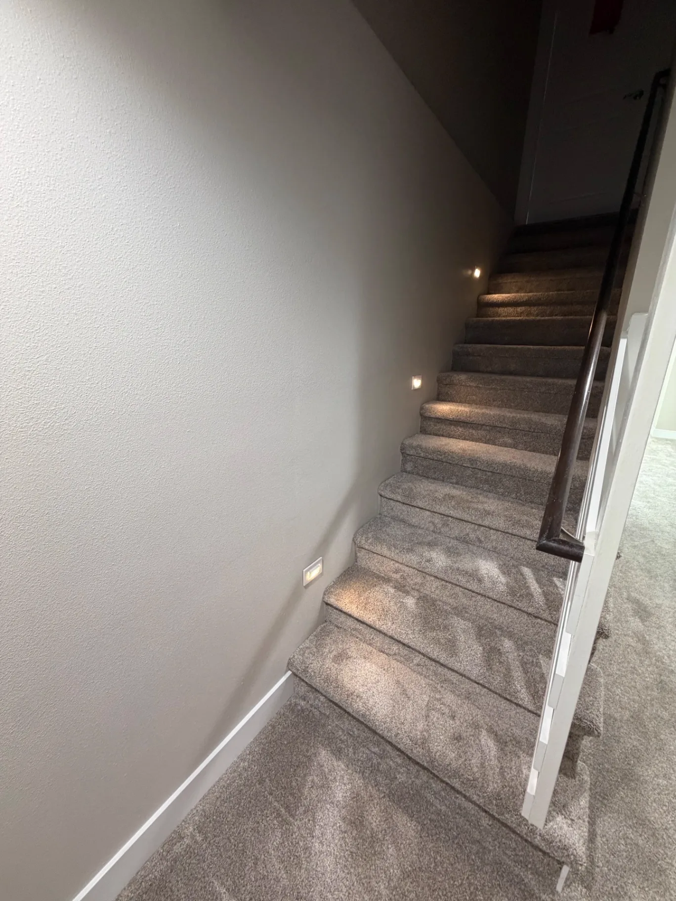 Carpeted stairway with fresh paint, white trim, stained handrail, and recessed step lighting