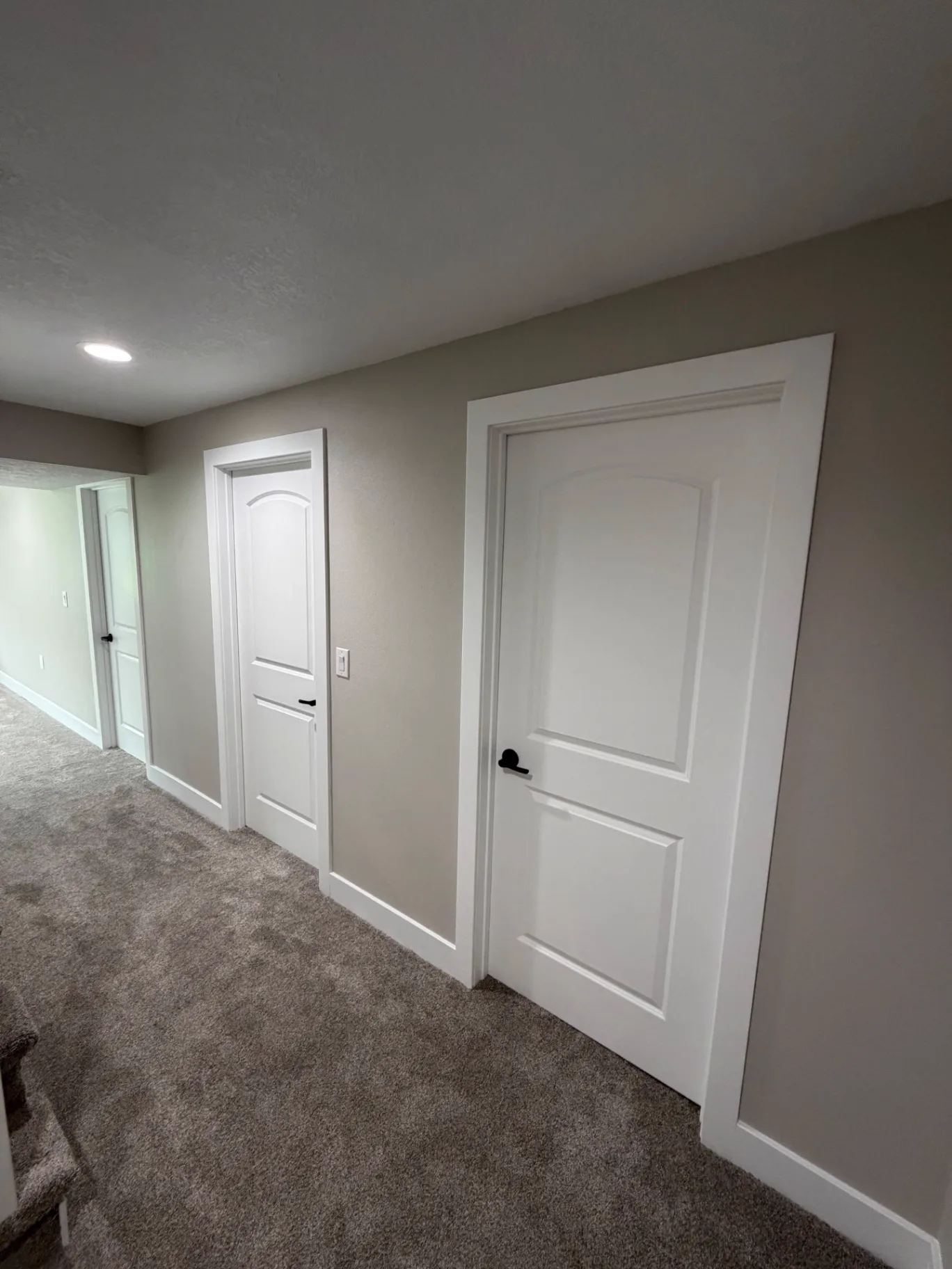 Finished lower level hallway with new white arch-panel doors, black lever hardware, painted trim, and new carpet