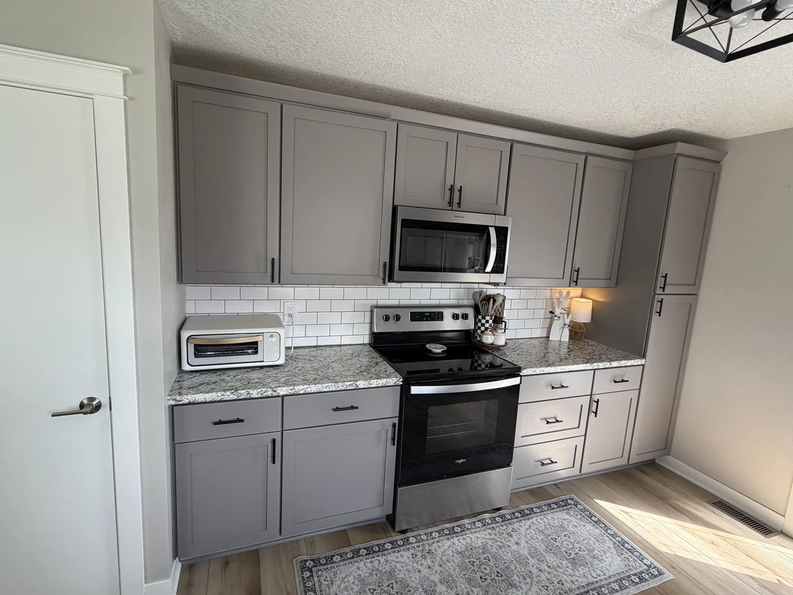 Remodeled kitchen with gray shaker cabinets, granite countertops, white subway tile backsplash, and black hardware
