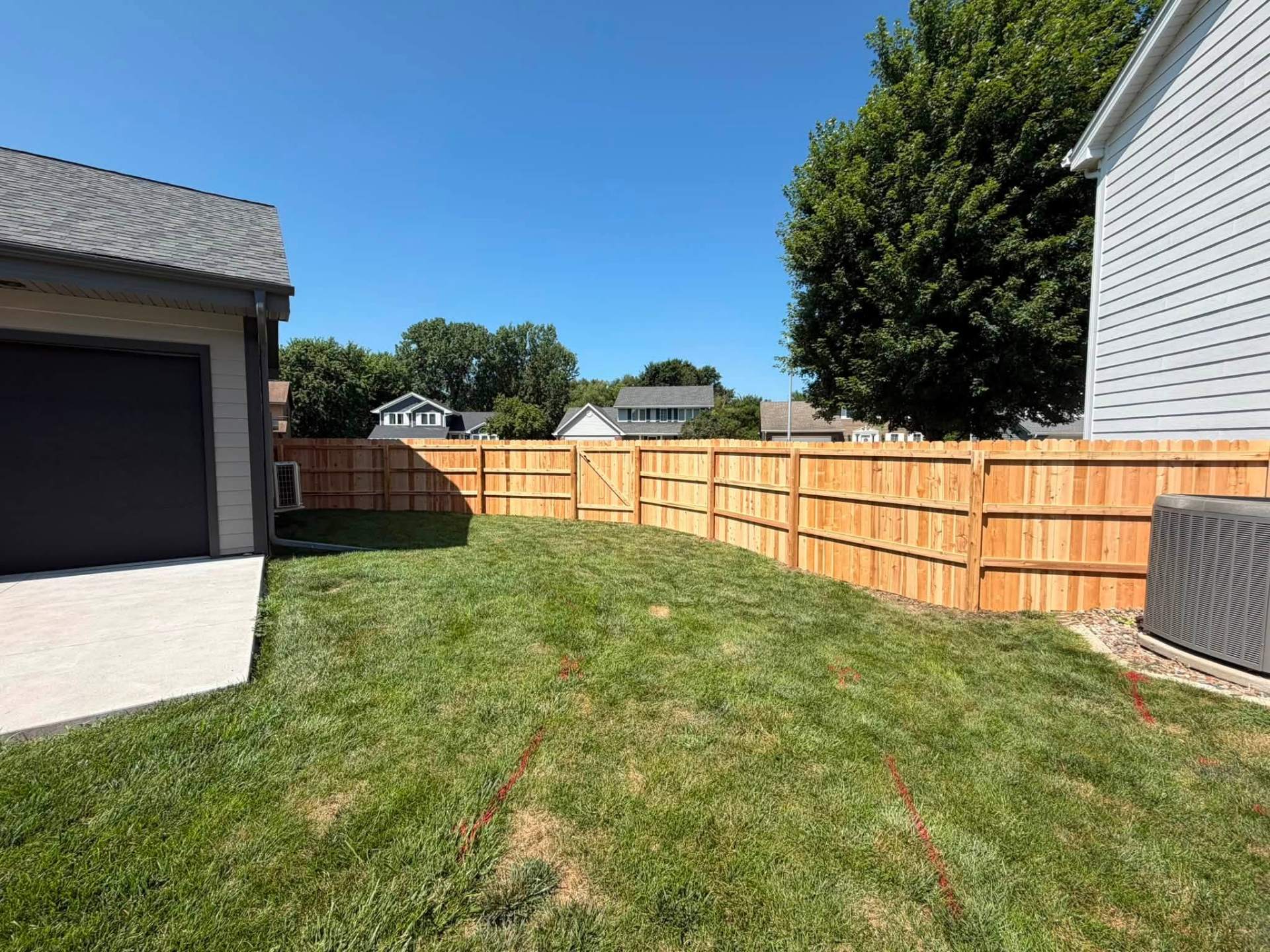 Backyard cedar privacy fence with a gate and rock border wrapping the property line beside a detached garage
