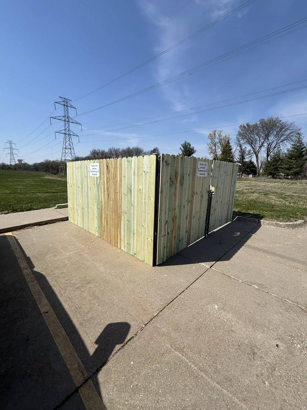 Pressure-treated dog-ear privacy fence enclosure with a gate built on a concrete pad in an open commercial lot