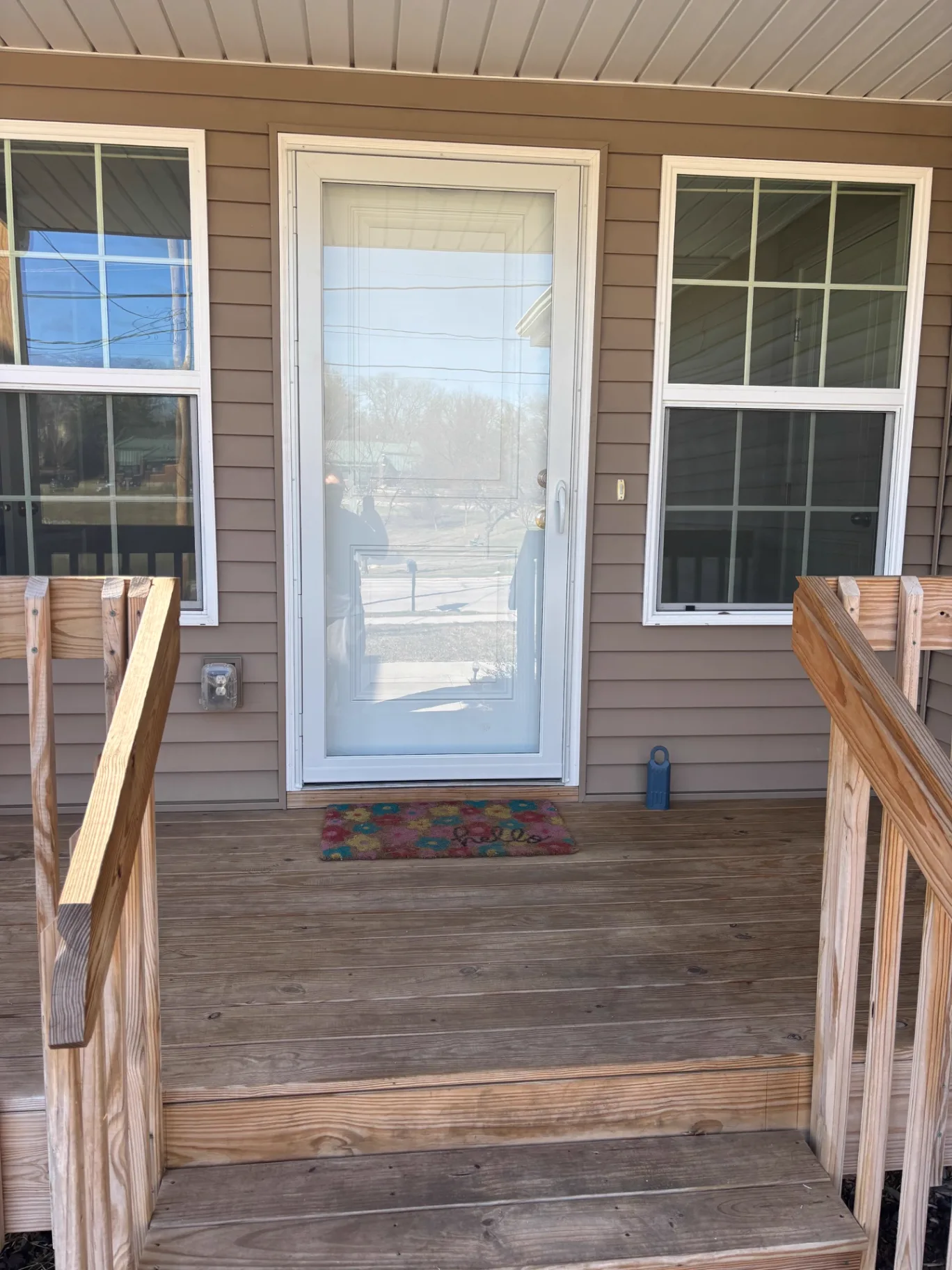 New white full-view exterior entry door with fresh trim and flanking grid windows above a wood deck landing and stairs