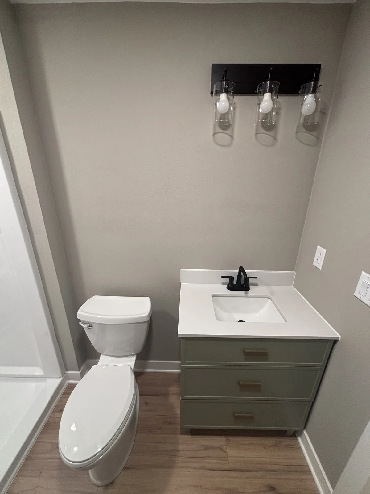 Finished bathroom with a sage green vanity, white quartz top, black faucet, and a three-light black vanity fixture