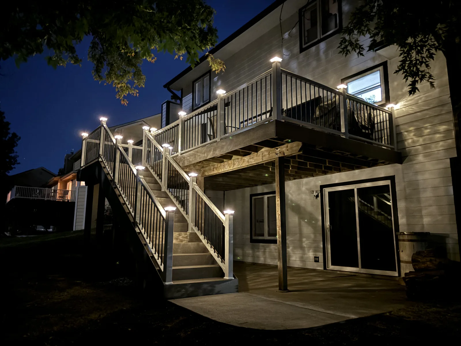 Elevated deck at night with lit post caps along the railing and a long lighted stair run down to a concrete patio