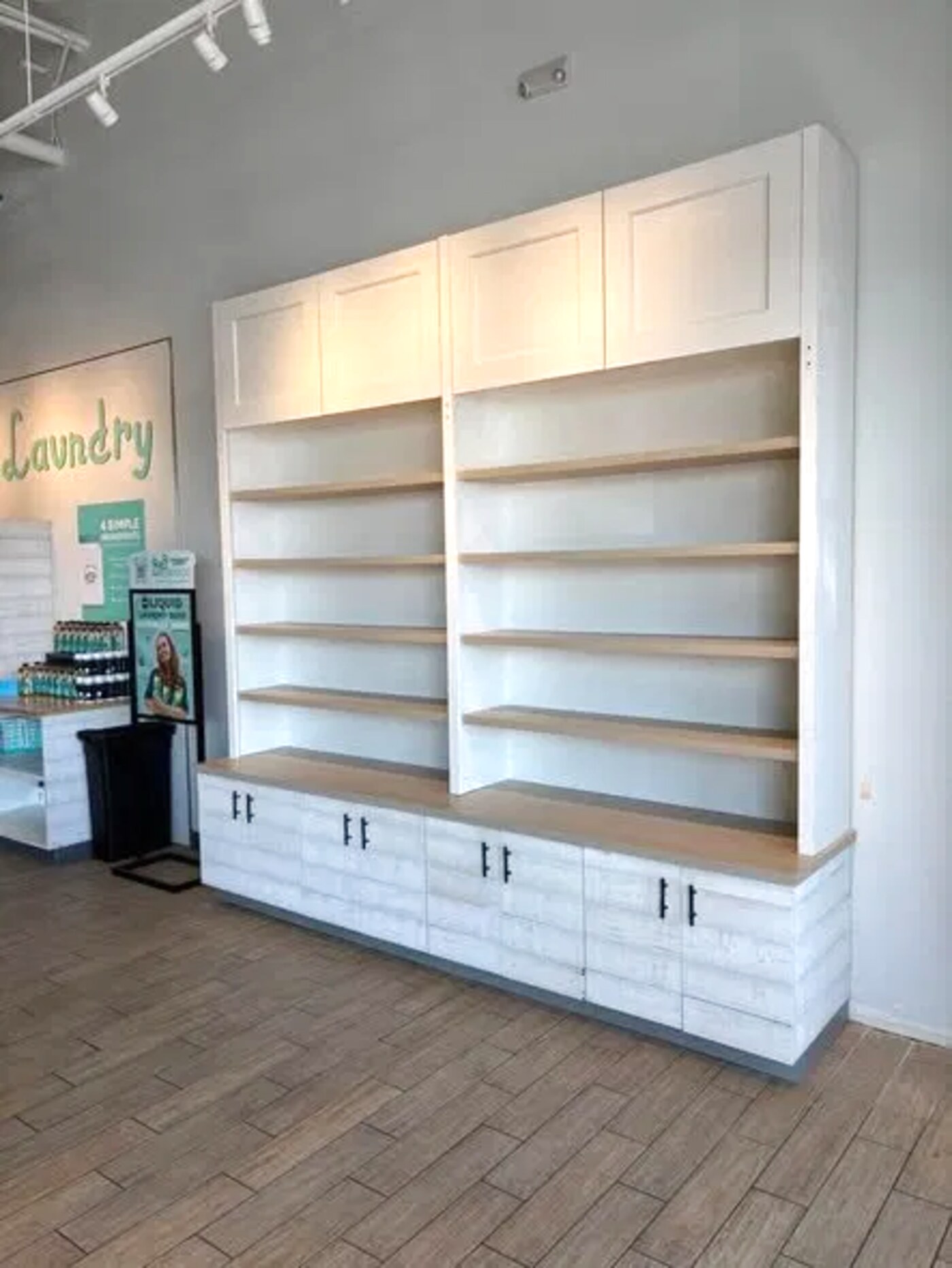 Floor-to-ceiling white built-in shelving unit with wood shelves and base cabinets