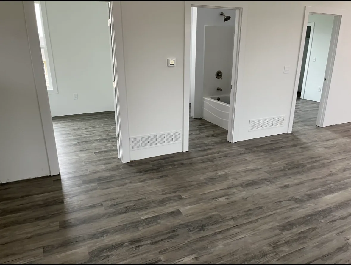 Freshly finished interior with gray wood-look vinyl plank flooring running through open doorways to a bathroom with a soaking tub