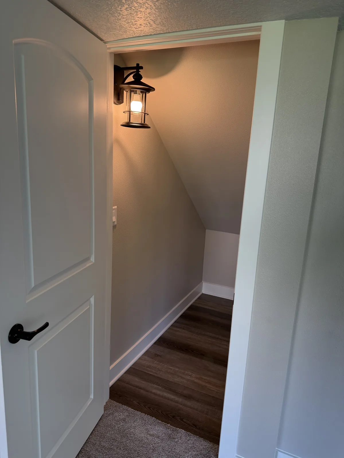 Finished under-stair nook with fresh paint, white trim, wood-look plank flooring, and a lantern-style wall sconce