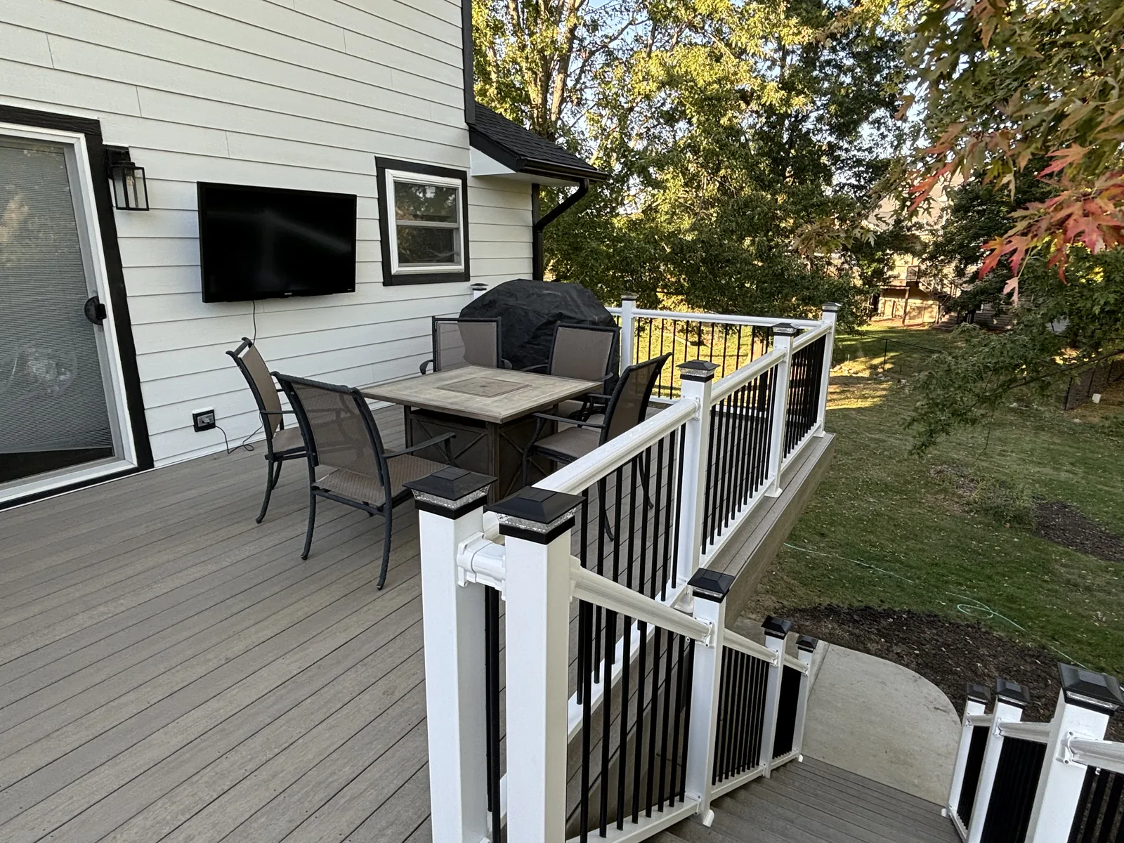 Composite deck with white railing, black metal balusters, solar post caps, and a stair run down to the yard