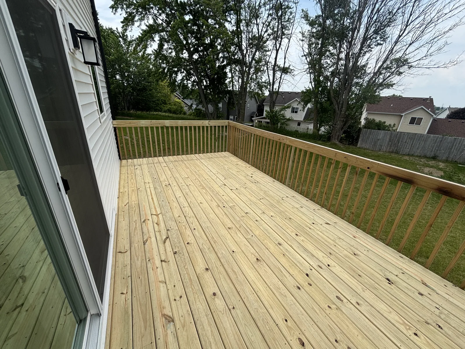 Newly built pressure-treated deck with full railing off the back of a white sided home overlooking the yard