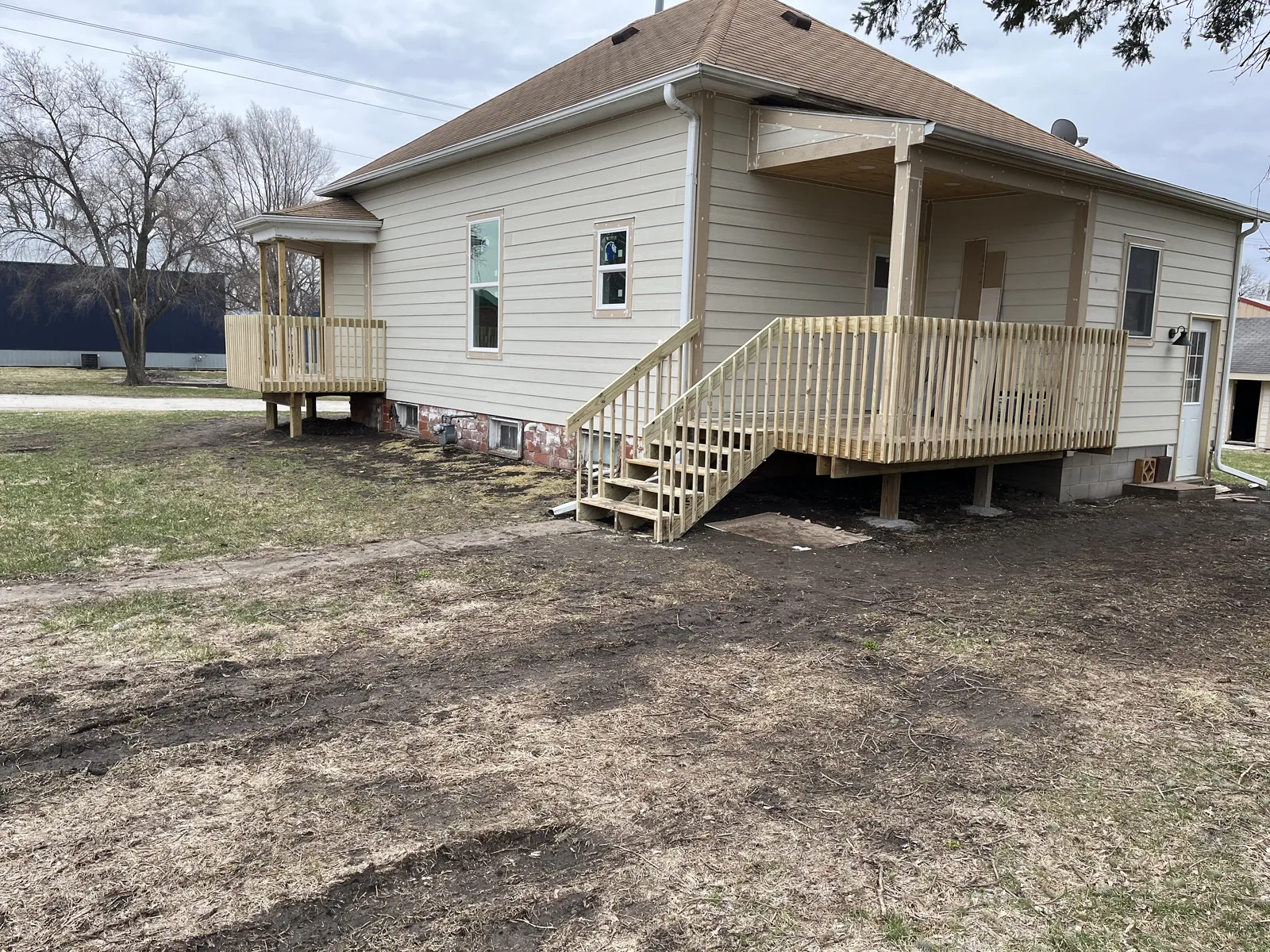 Raised deck with wood railing and stair run attached to the side of a tan house