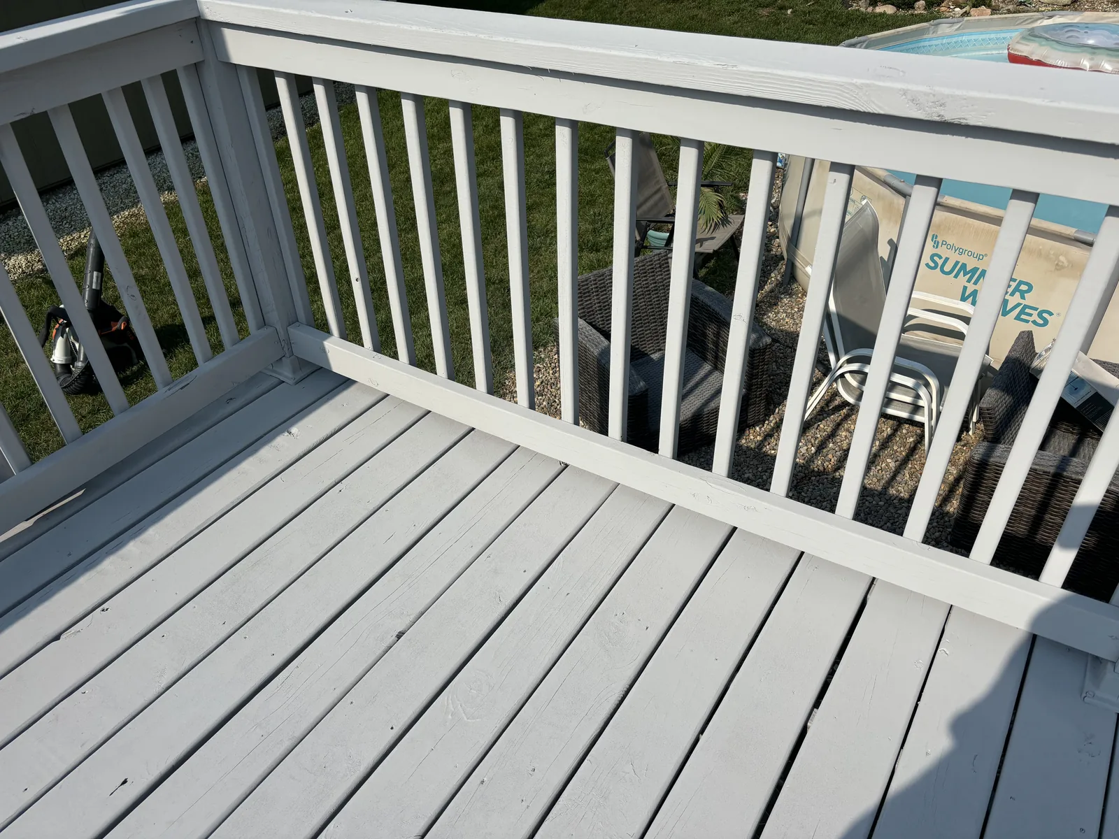 Freshly painted white deck corner with railing overlooking a backyard patio and above-ground pool