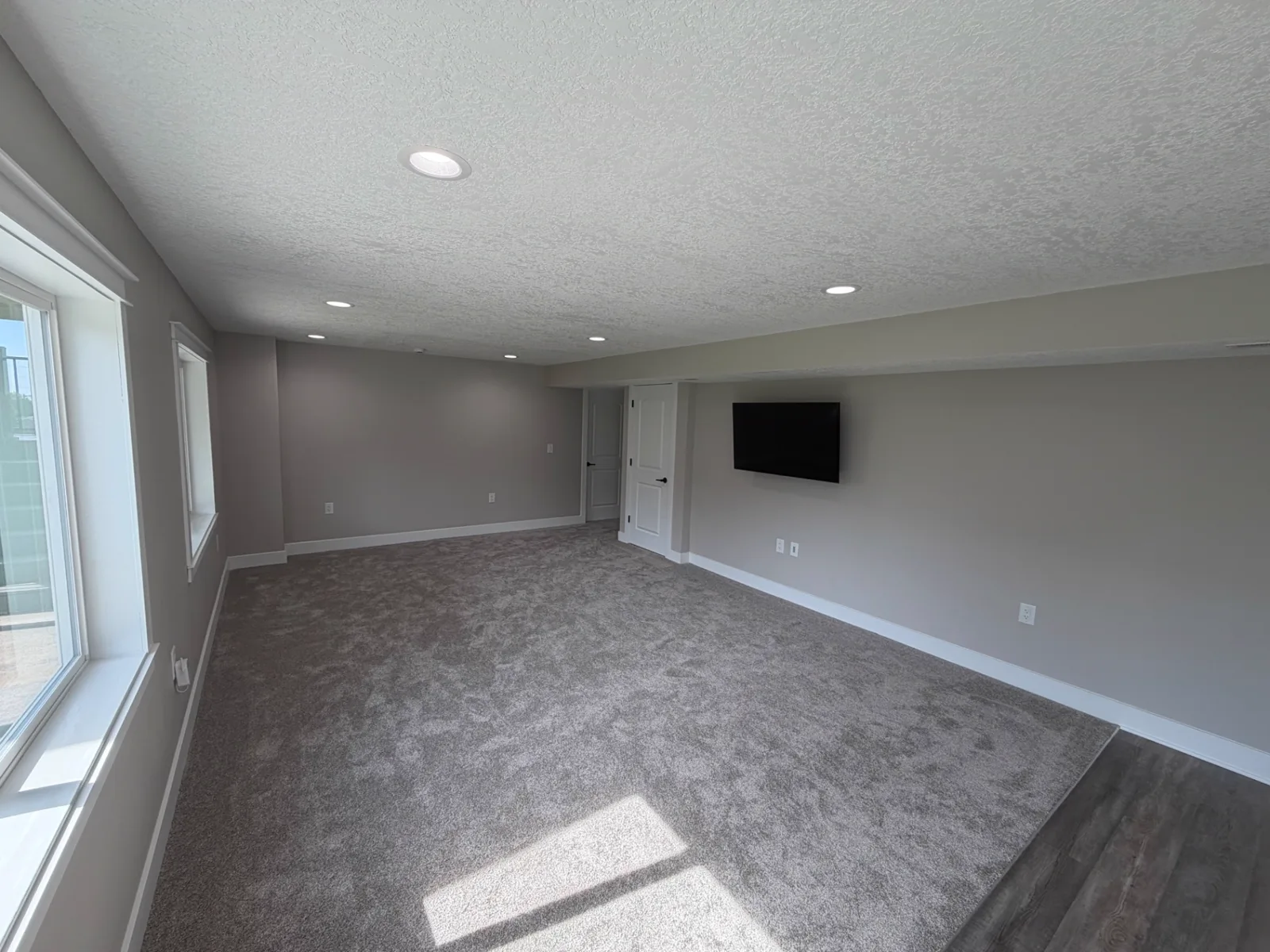 Finished basement living area with painted walls, recessed lighting, new carpet, and a wall-mounted television