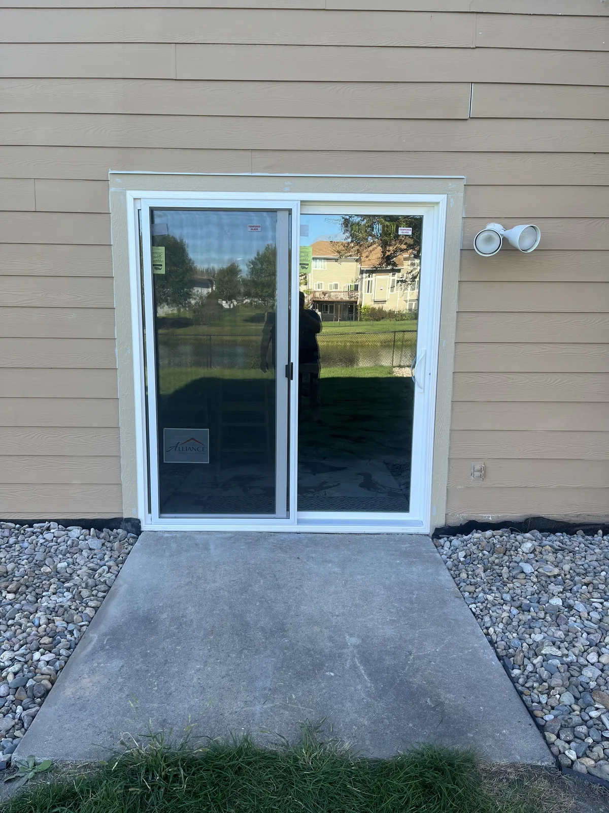 Newly installed white sliding patio door with a concrete pad and rock border at a walkout basement