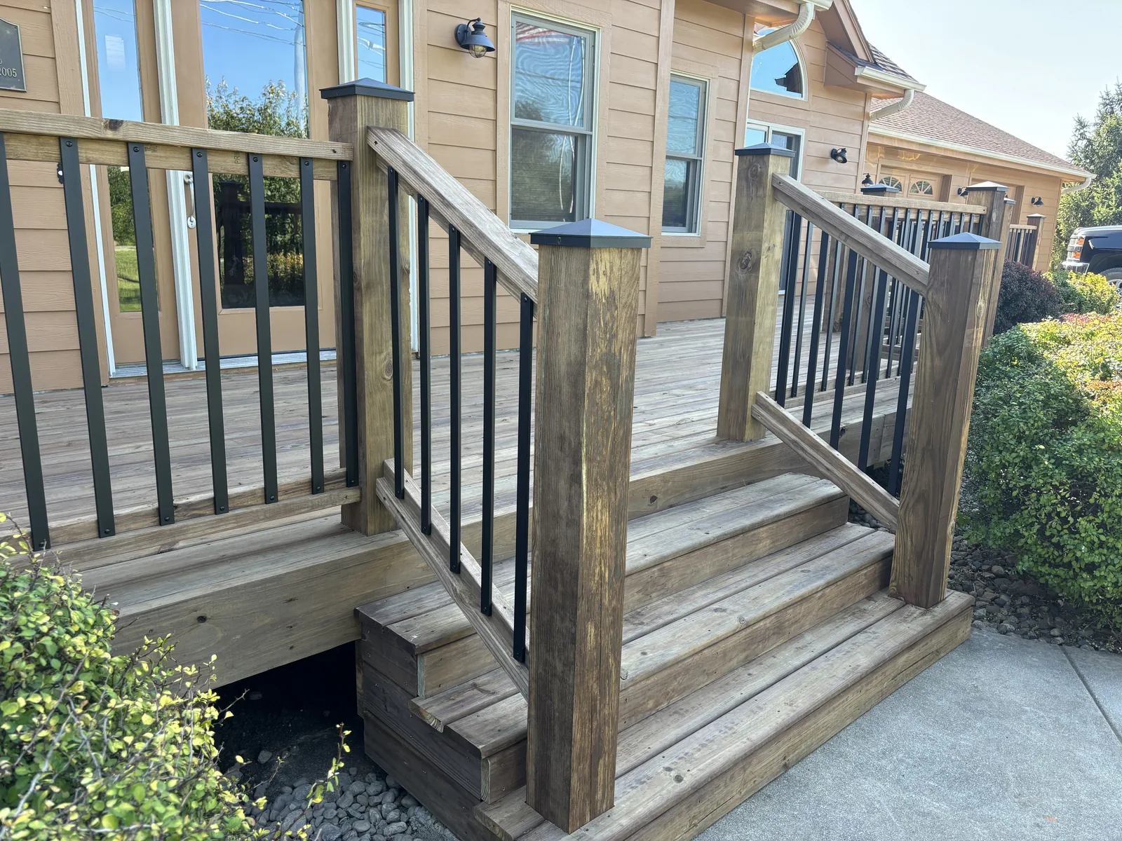 Wood deck stairs with a matching wood handrail and black metal balusters leading up to a front entry