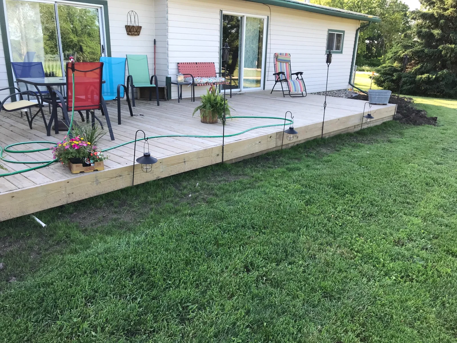 Newly built ground-level pressure-treated deck spanning the back of a white sided home with patio door access
