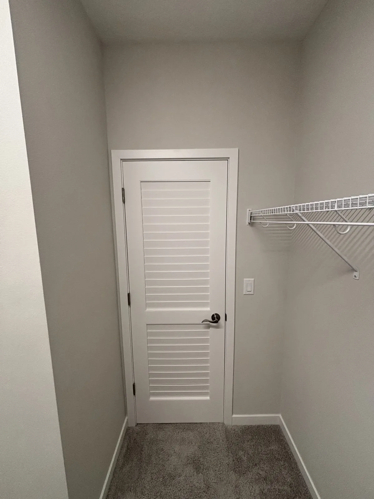 Finished walk-in closet with painted walls, white louvered door, wire shelving, and new carpet