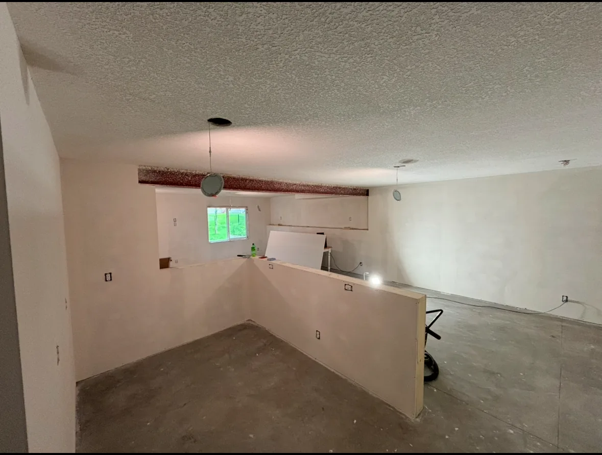Lower level with newly hung and finished drywall, textured ceiling, and a half-wall partition ready for flooring