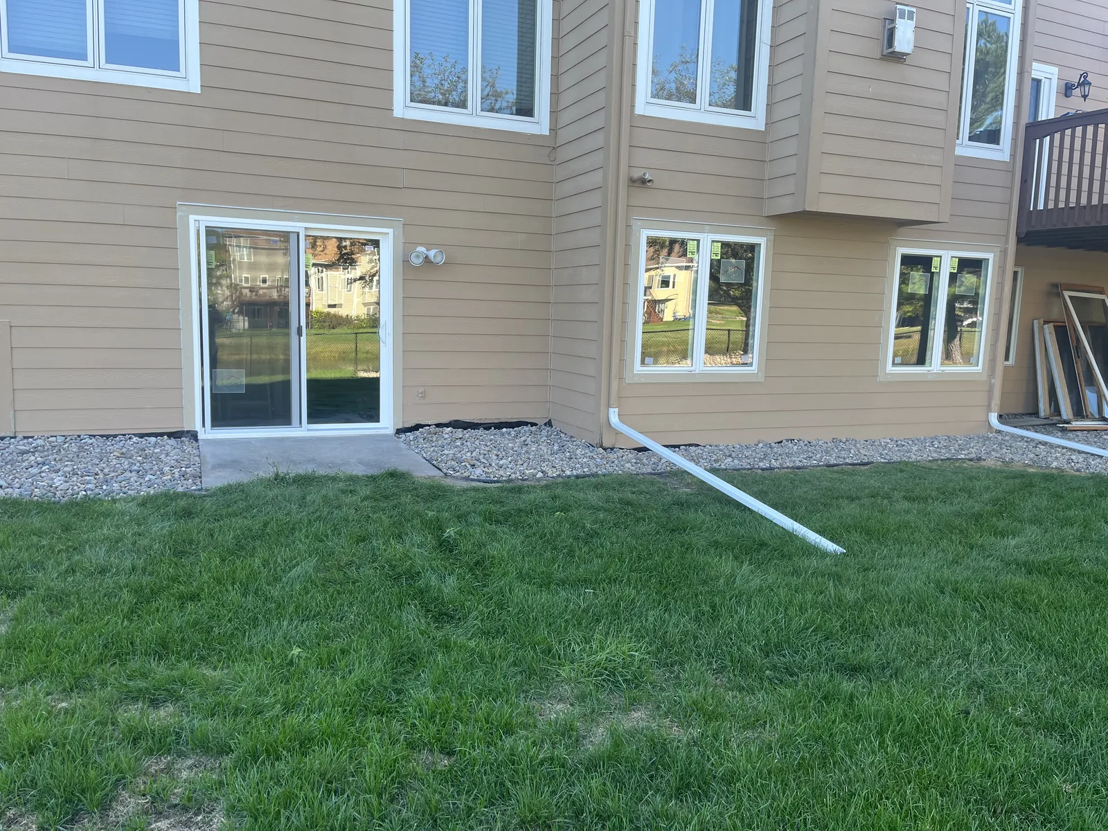 Rear of a home showing a new sliding patio door and basement windows installed in tan siding