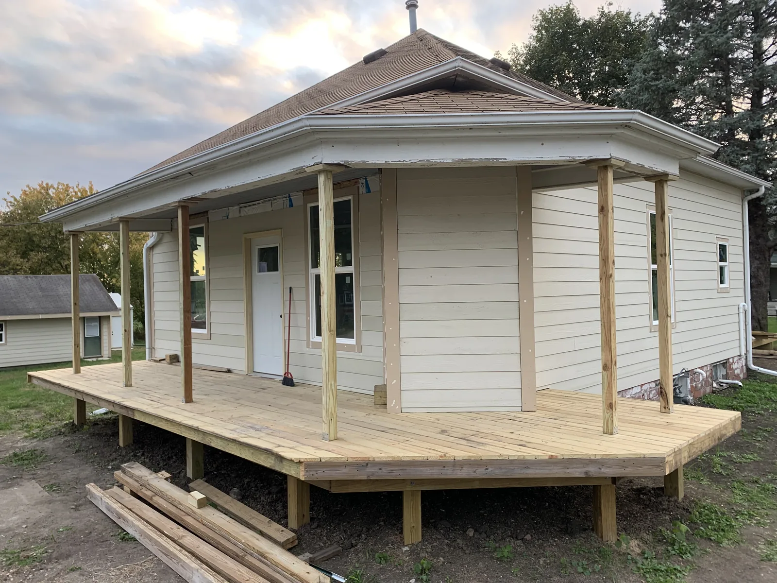 Newly framed wrap-around porch deck with support posts on a white sided house at sunset