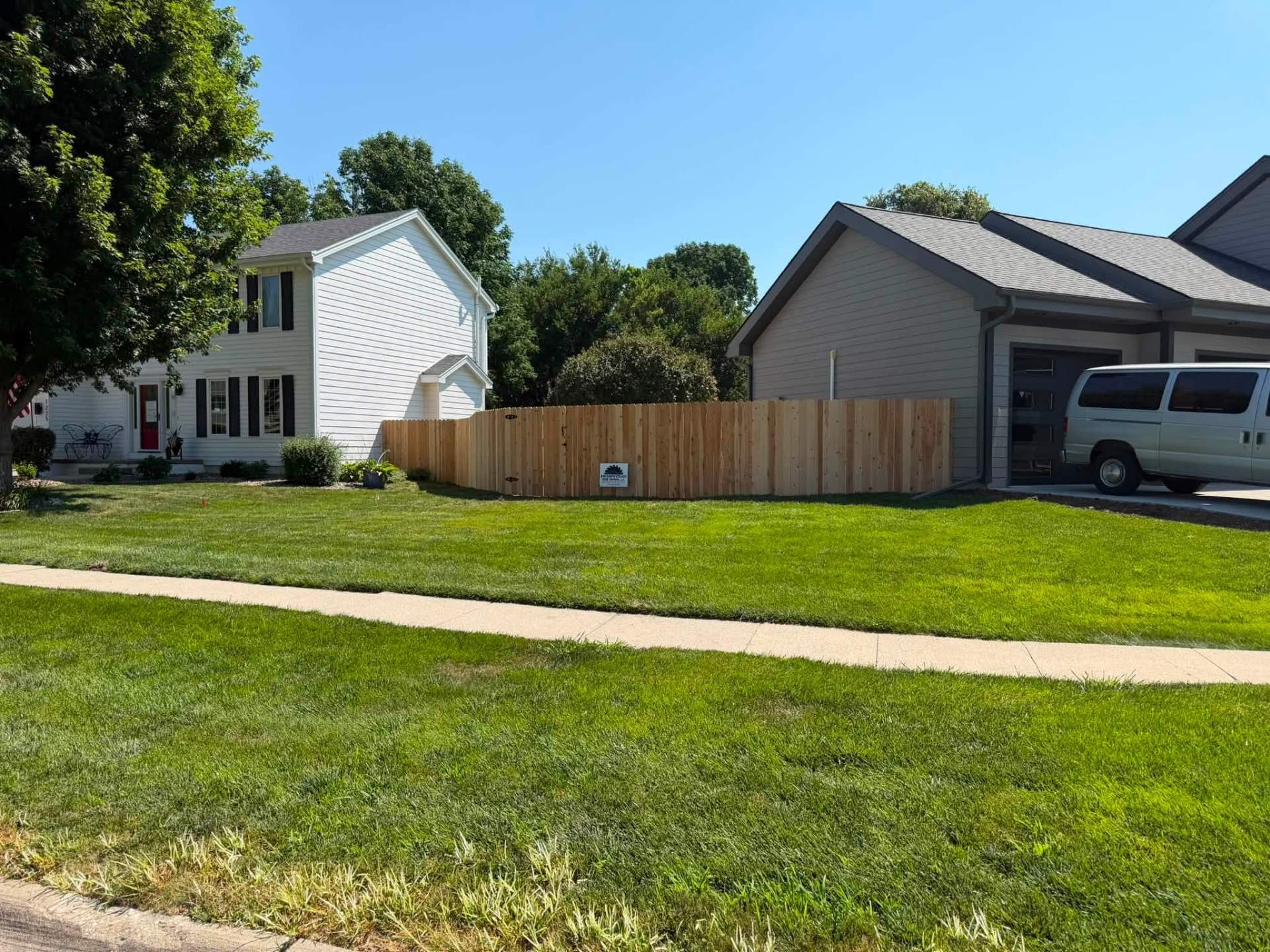 Street view of a new cedar privacy fence enclosing a side yard between a white two-story home and a neighboring garage