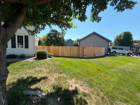 Cedar privacy fence with gate running between two homes, viewed across a shaded green lawn