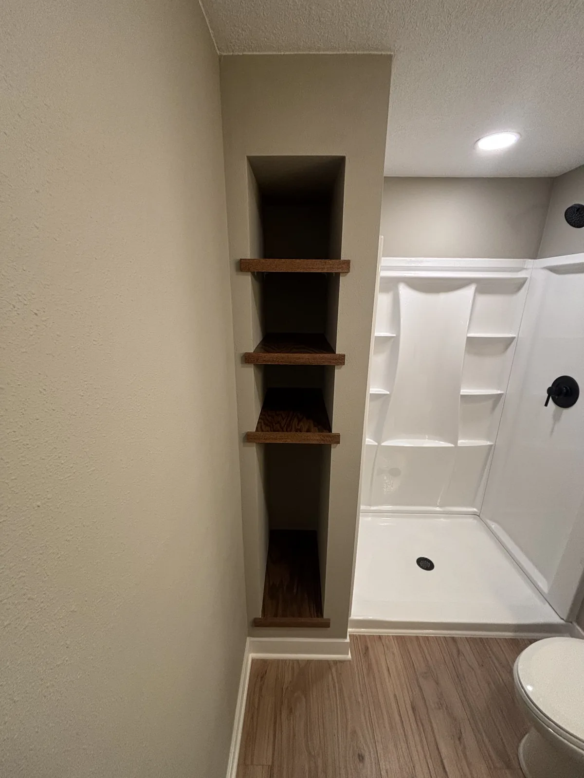 Bathroom with a new white shower unit, black fixtures, and a recessed niche with stained wood shelves