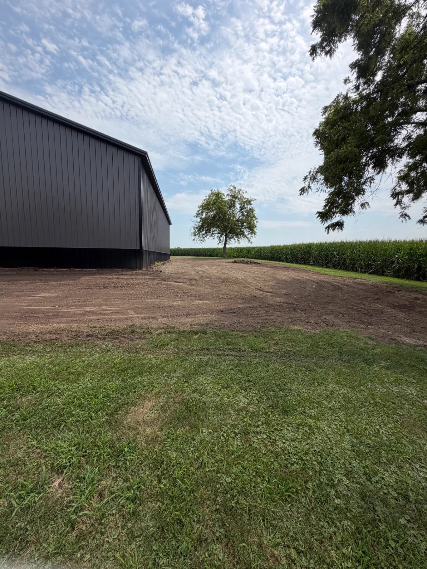 Graded dirt work and site prep wrapping around a new black post-frame building beside an Iowa corn field