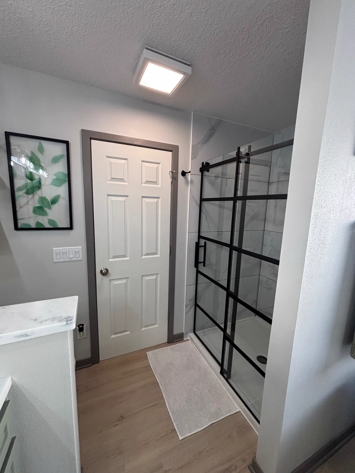Walk-in shower with marble-look tile walls and a black grid-framed sliding glass door beside a painted six-panel door