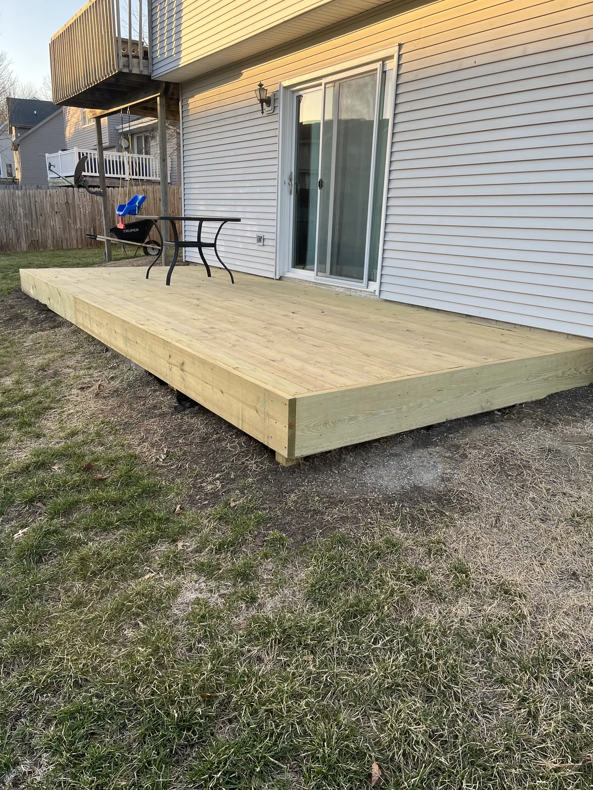 Large ground-level pressure-treated deck along the back of a white sided home