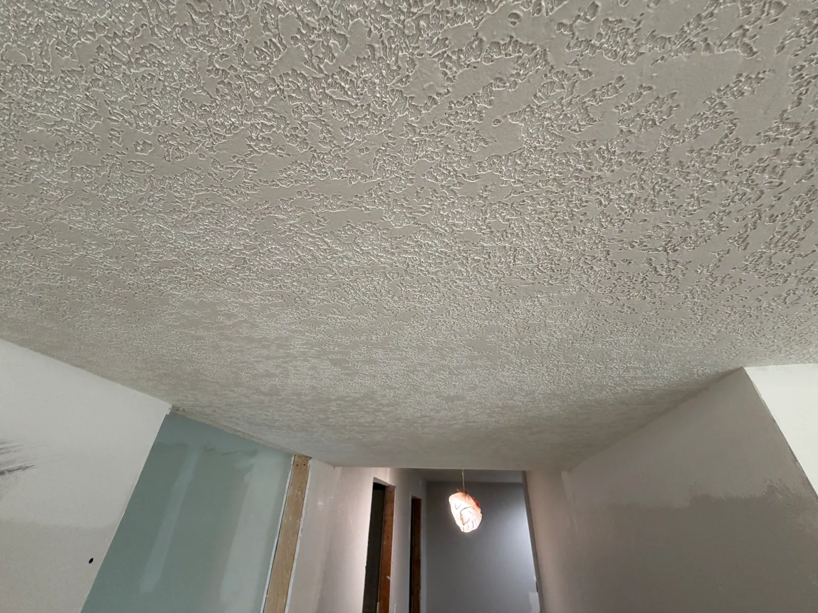 Freshly sprayed knockdown ceiling texture over a hallway with newly hung drywall below