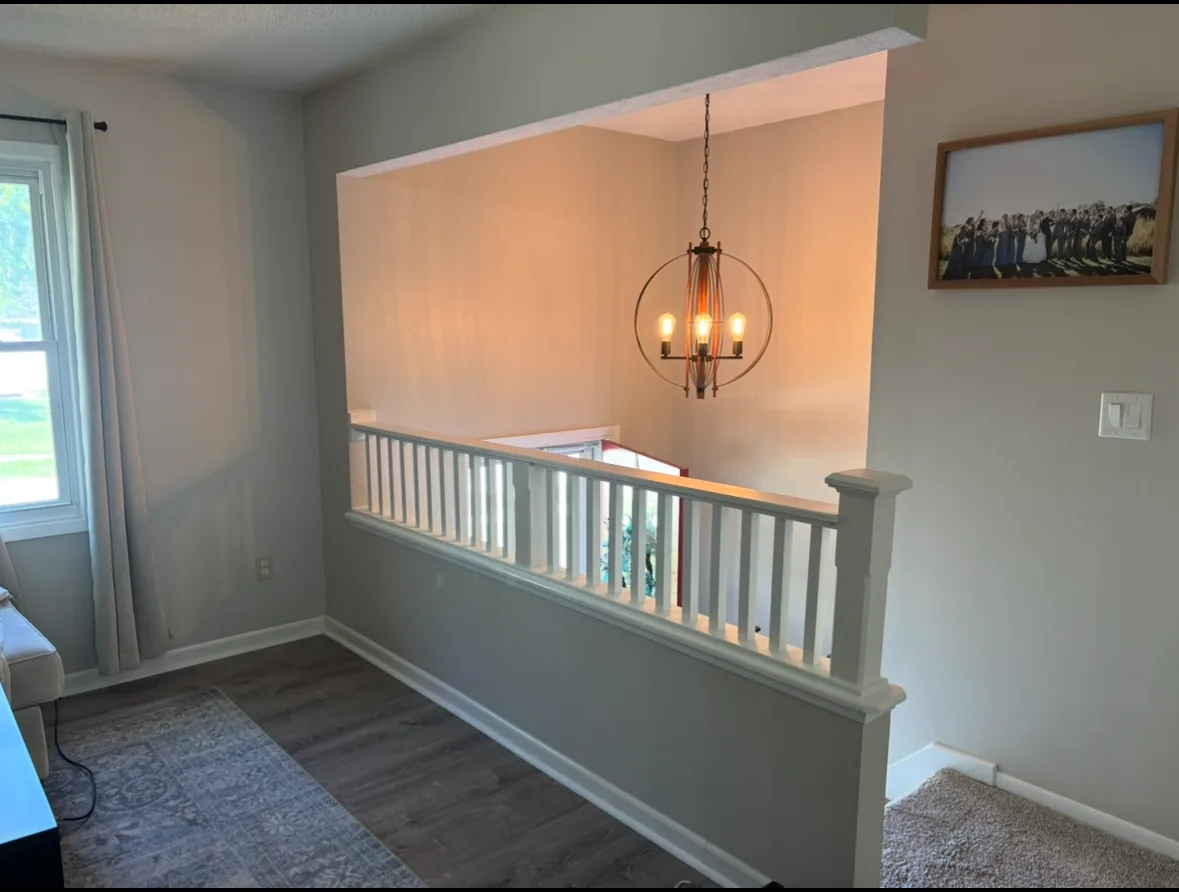Interior half-wall opening with white spindle railing and fresh paint overlooking a stairwell and chandelier