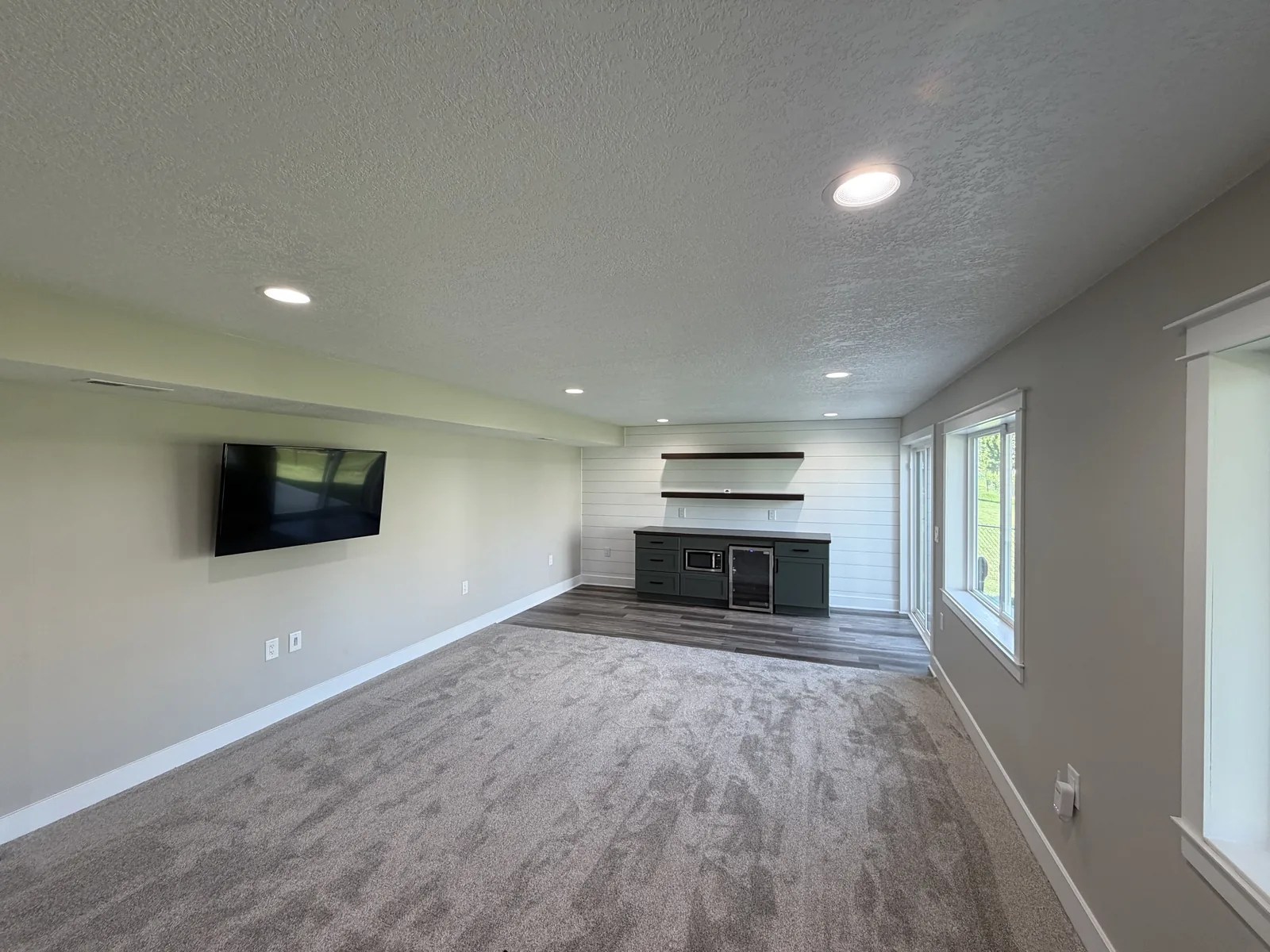 Finished basement family room with recessed lighting, new carpet, shiplap accent wall, and a built-in beverage center with floating shelves
