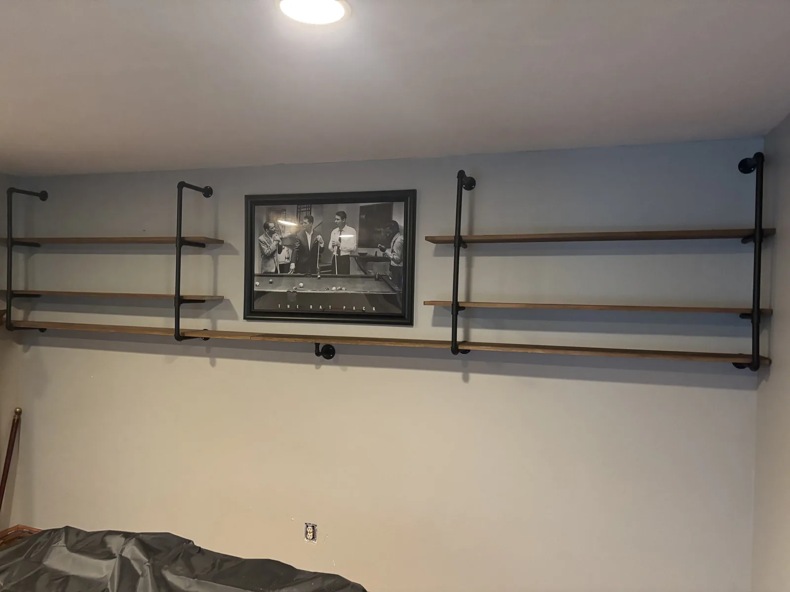 Basement wall with custom black pipe and stained wood open shelving mounted above a bar area