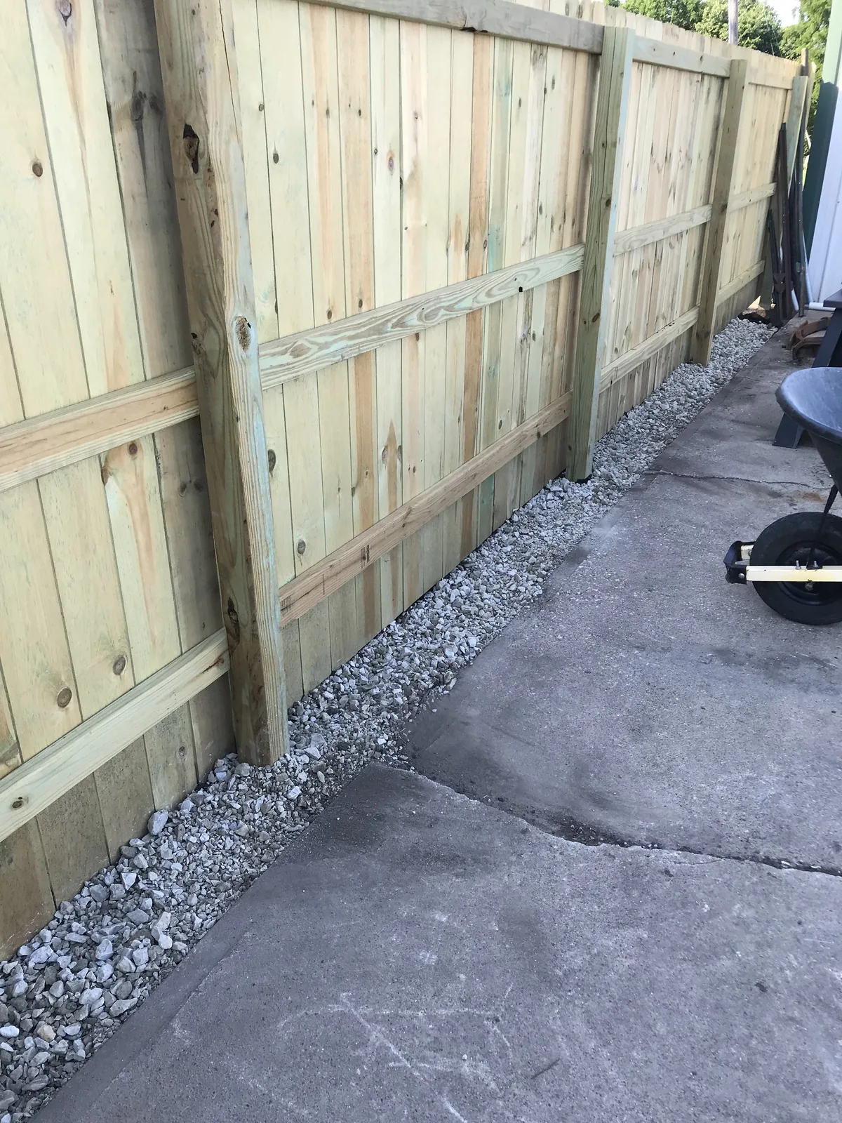 New pressure-treated privacy fence with a gravel drainage strip along a concrete driveway