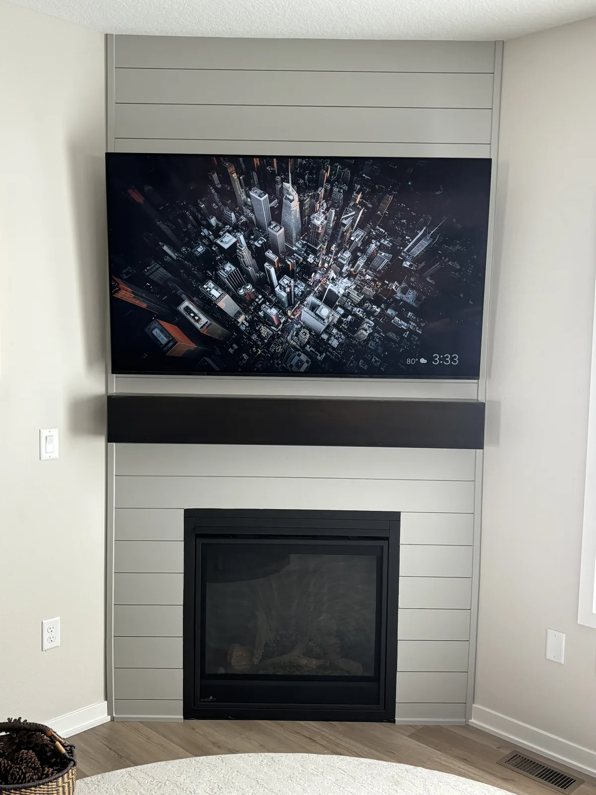 Corner fireplace surround finished in painted shiplap with a dark stained mantel and a wall-mounted television above